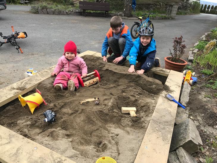 Tre barn leker i en stor sandkasse.