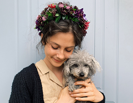 Ung kvinne med blomster i håret som holder på en liten hund.