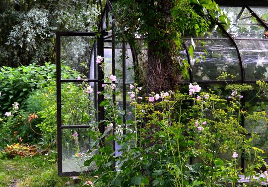 Veksthus i en frodig hage omkranset av blomster