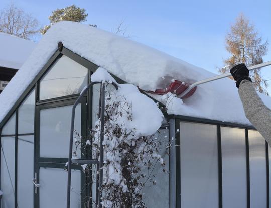 Måker snø av et veksthustak med snøskuffe